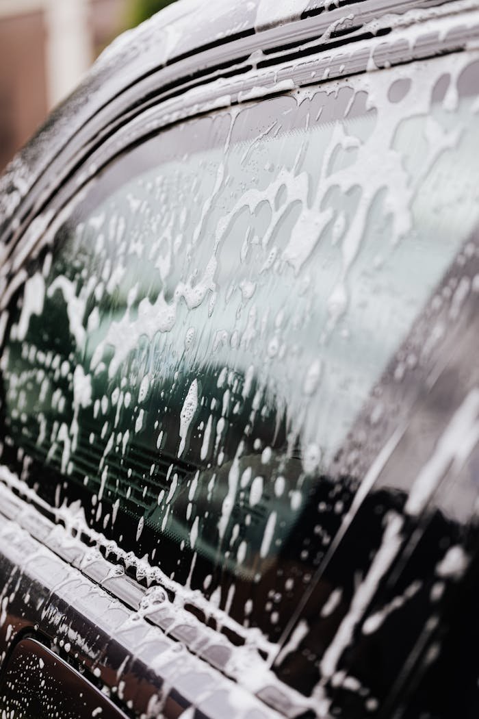 Detailed view of a black car window covered in soap suds during a wash. Perfect for car care themes.