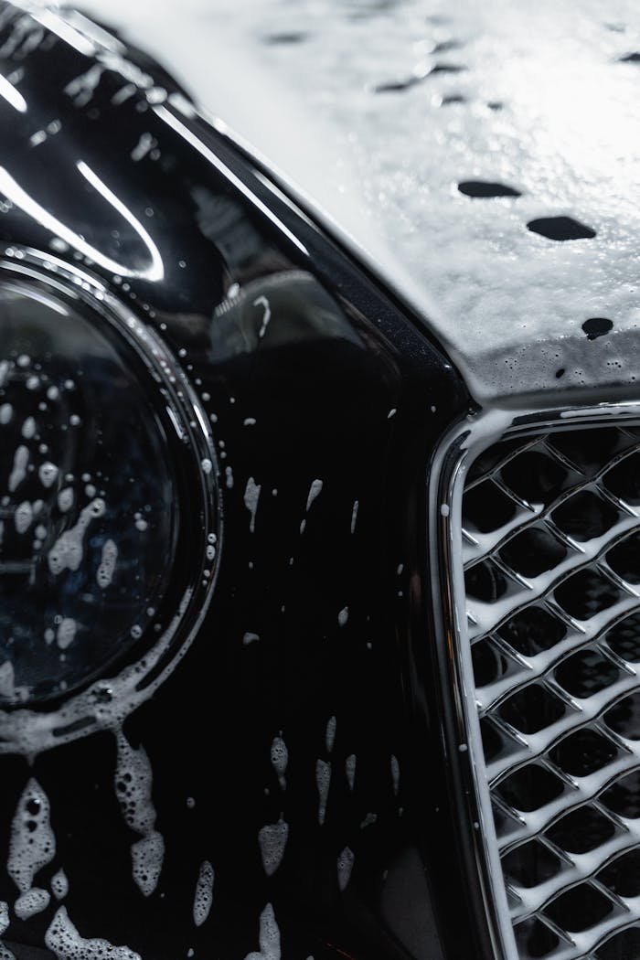 Detailed view of a luxury black car covered with soap suds during a wash.